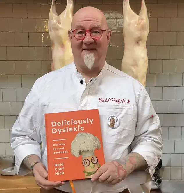 Photo of chef Nick Jaye in a kitchen holding his book Deliciously Dyslexic